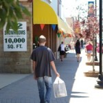 A man walking on a road wearing a black t-shirt and carrying a package